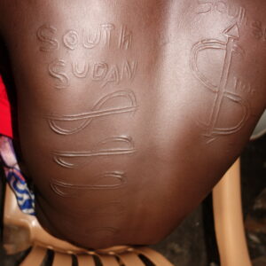Young man from Kurenen age-set, nyakeno called Koliyam (SPLA) represented by scarifications of 'South Sudan' inscribed on the body, along with SPLA symbols such as the sign for Division 2 and Division 8. Manyirany, June 2022 (photo by Lauryen Oleyo).